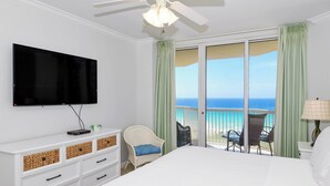 Habitación de hotel con cama, televisión, cómoda, una silla y balcón con vista al océano.