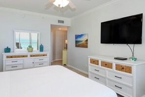 A bedroom with a bed, white dresser, television, and a painting of a beach.