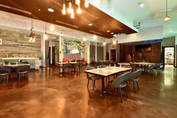 A spacious dining area with multiple tables and chairs, a wooden wall, and hanging light fixtures.