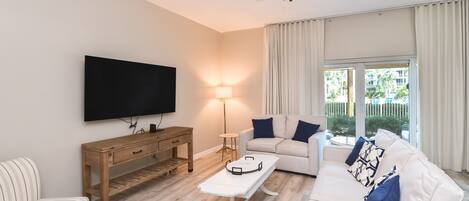 Un salon moderne doté d’un téléviseur à écran plat, de meubles en bois, d’un canapé blanc avec des coussins bleus et d’un ventilateur de plafond.