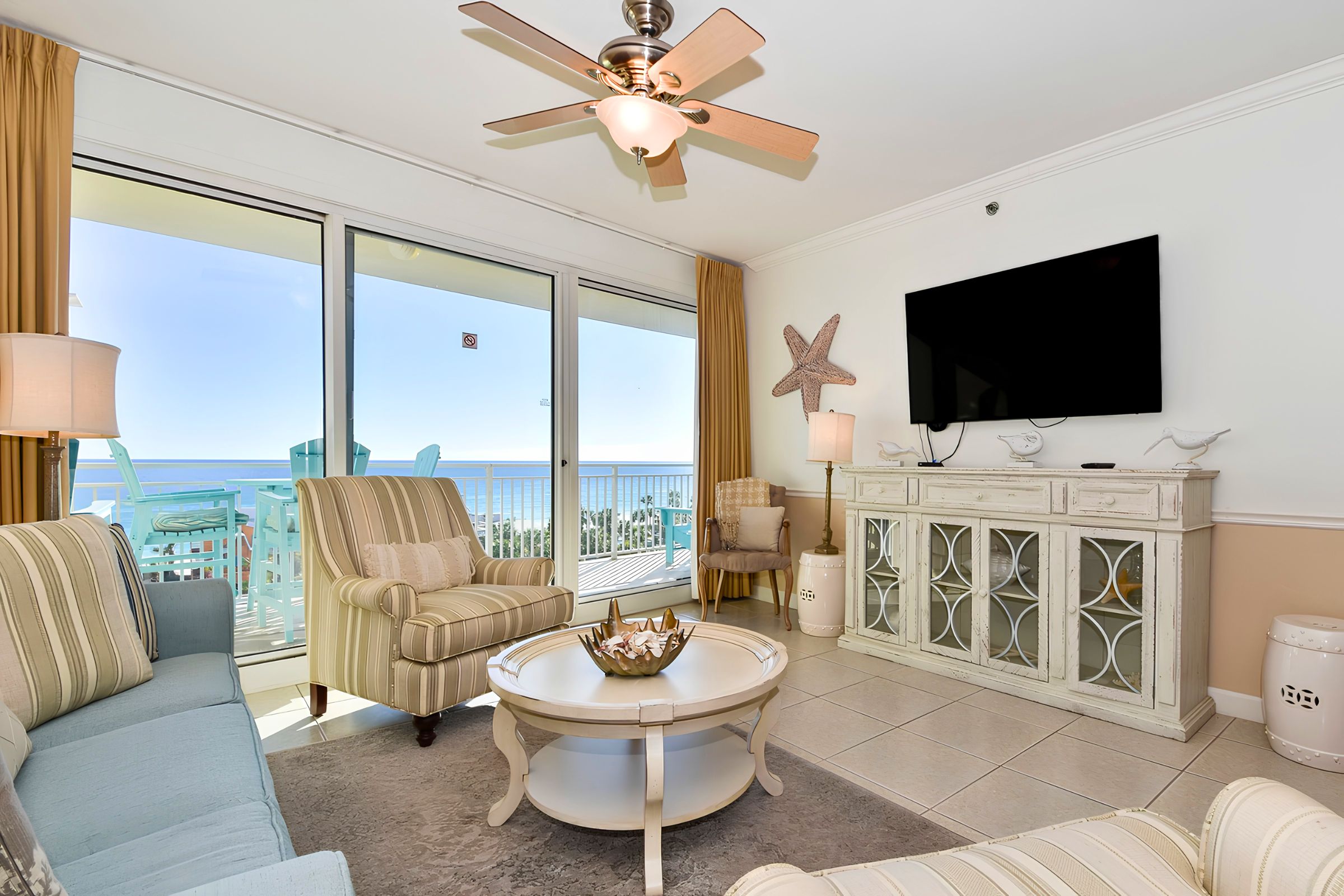 A spacious living room with a large window, a ceiling fan, a television, and a decorative cabinet.