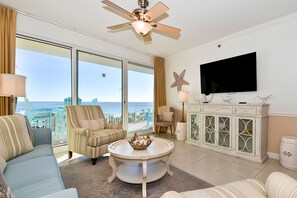 Ein geräumiges Wohnzimmer mit großem Fenster, Deckenventilator, Fernseher und einem dekorativen Schrank.