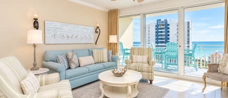 A spacious living room with a blue sofa, striped armchairs, a round coffee table, and a ceiling fan.