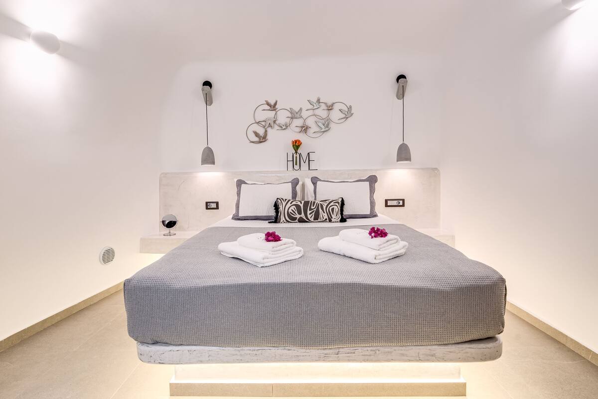 A modern bedroom with a large bed, a wall-mounted artwork, and a small table with a vase.