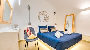 A bedroom with a bed, a chair, a mirror, and a wall art piece. - Tiara Suites (Santorini)