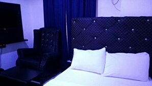 A hotel room with a bed, a chair, and a TV mounted on the wall. - SMD Hotel and Suites (Port Harcourt)