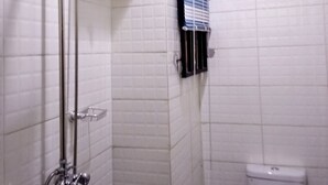 A bathroom with white tiled walls, a shower with a handheld showerhead, a toilet, and a window with blinds. - SMD Hotel and Suites (Port Harcourt)
