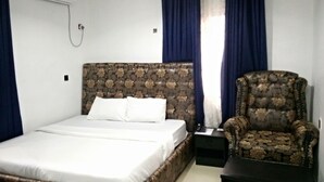 A bedroom with a bed, a chair, a nightstand, and a wall-mounted air conditioner. - SMD Hotel and Suites (Port Harcourt)