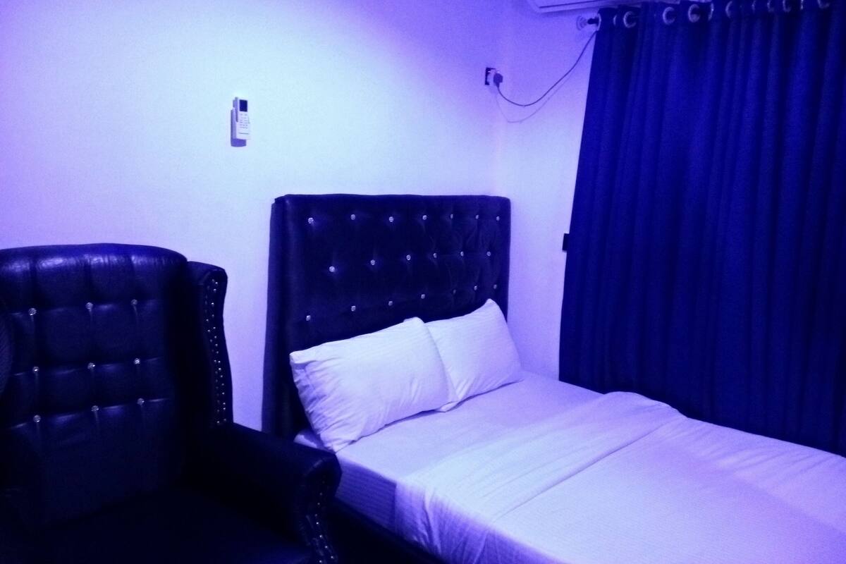 A room with a bed, a chair, and an air conditioning unit on the wall.
