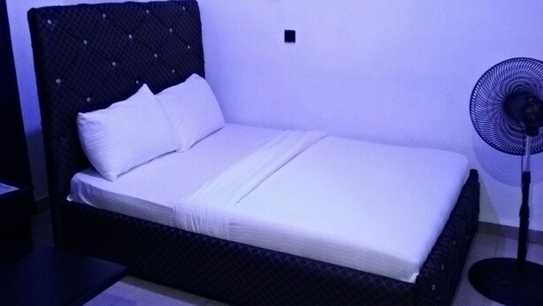 A single bed with a dark headboard and white bedding in a room with a tiled floor. - SMD Hotel and Suites (Port Harcourt)