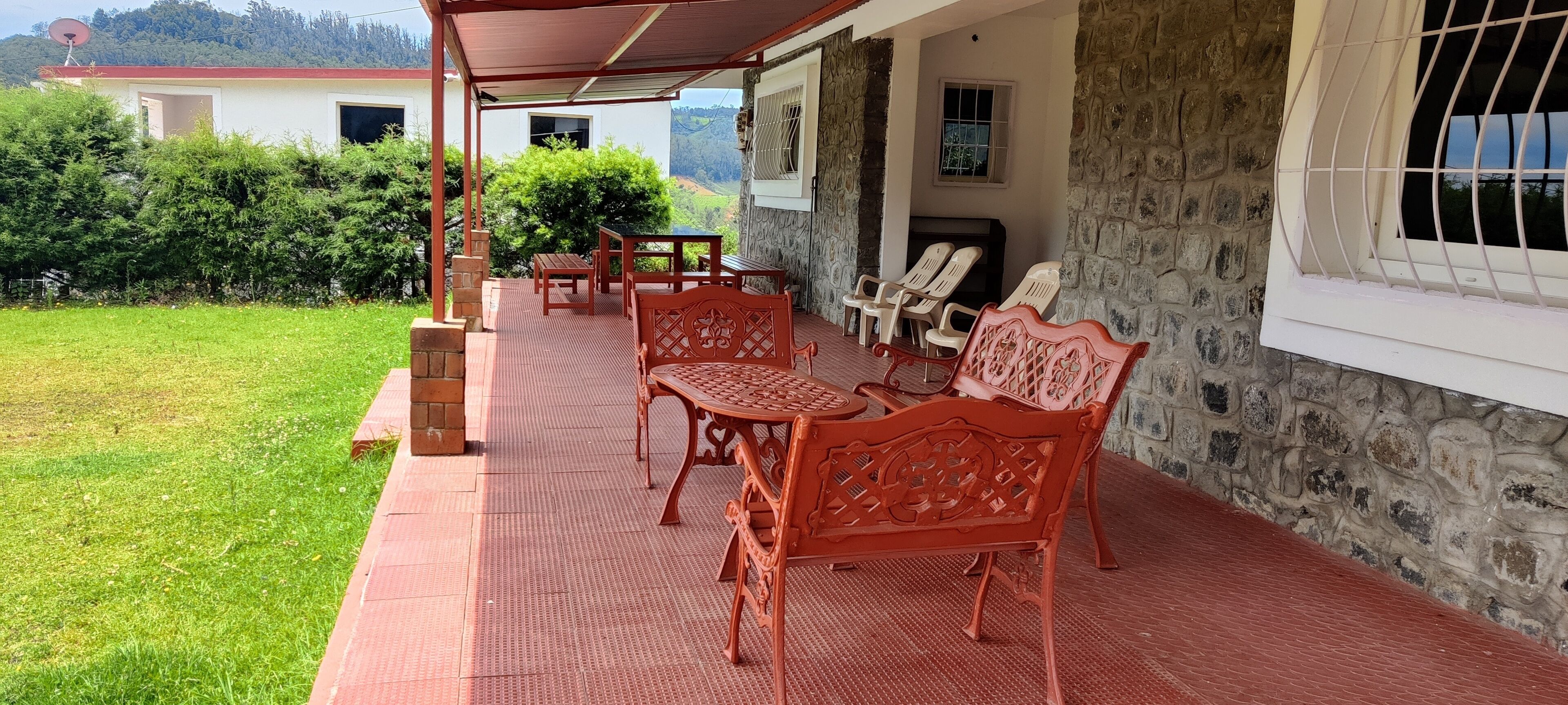 A covered outdoor seating area with red benches and tables, a stone wall, and a view of a hillside.