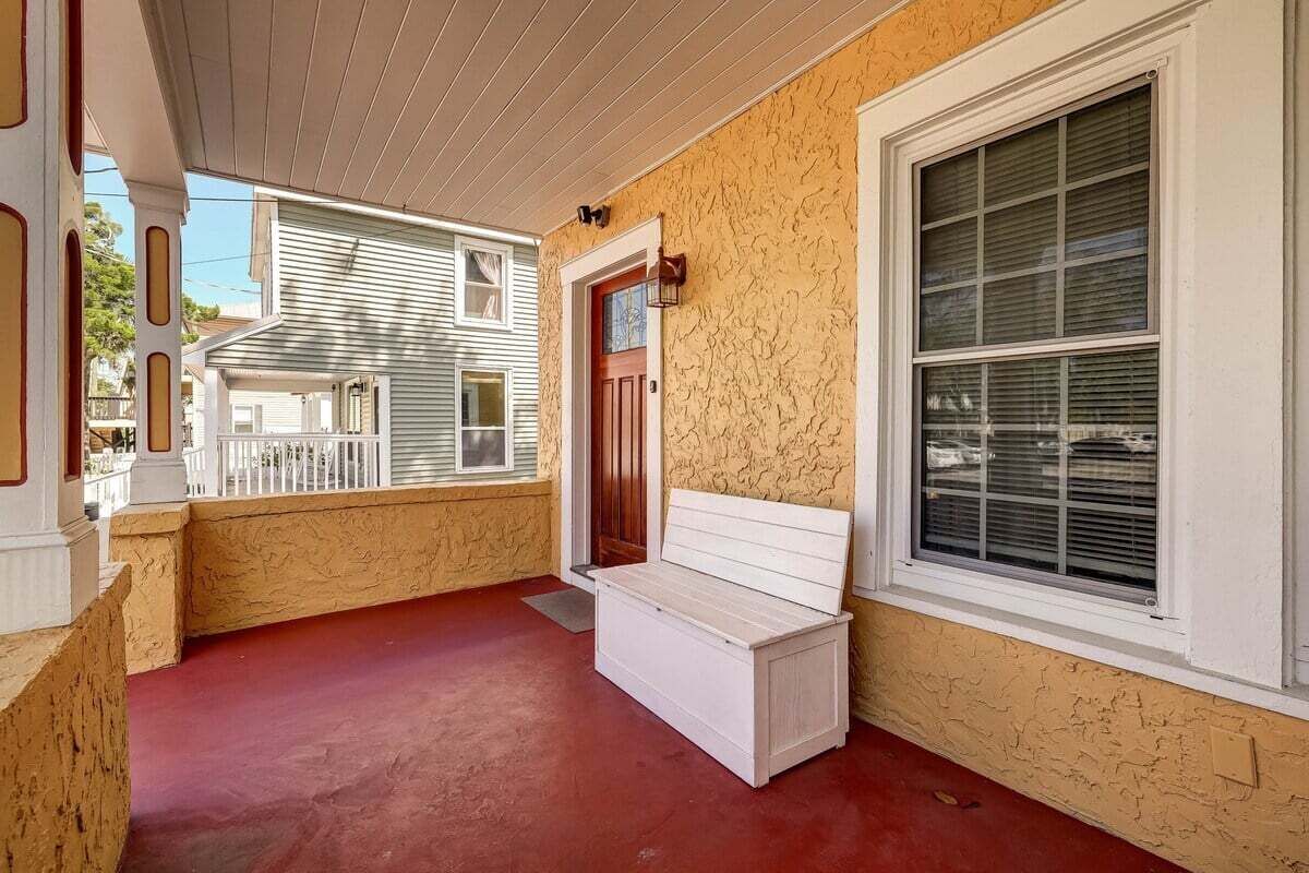 Ein überdachter Balkon mit einer Bank, einer Tür und einem Fenster.