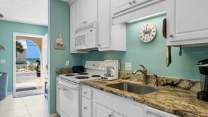 A kitchen with white cabinets, a granite countertop, a stainless steel sink, a microwave, a stove, and a coffee maker. - Steps to beach w/ pool and daily attraction perks (Panama City Beach)