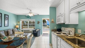 A kitchen with white cabinets, a stove, and a microwave. There is a dining area with a table and chairs. - Steps to beach w/ pool and daily attraction perks (Panama City Beach)