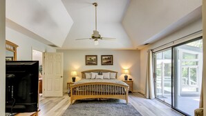 A bedroom with a bed, a ceiling fan, two bedside lamps, a large window, and a sliding glass door leading to a balcony. - Sunset Rentals | Off Shore 16 (Hilton Head Island)