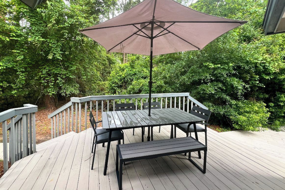 A wooden deck with a table and chairs, surrounded by lush greenery.