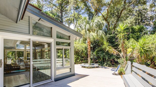 A modern house with large glass doors, a wooden deck, and a lush garden with palm trees. - Sunset Rentals | Off Shore 16 (Hilton Head Island)