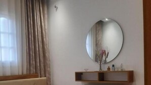 Un dormitorio con una cama, un espejo redondo, un radiador y una alfombra a rayas coloridas.