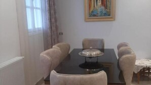 Un comedor con una mesa negra, seis sillas tapizadas, un cuadro en la pared y una ventana con cortinas.