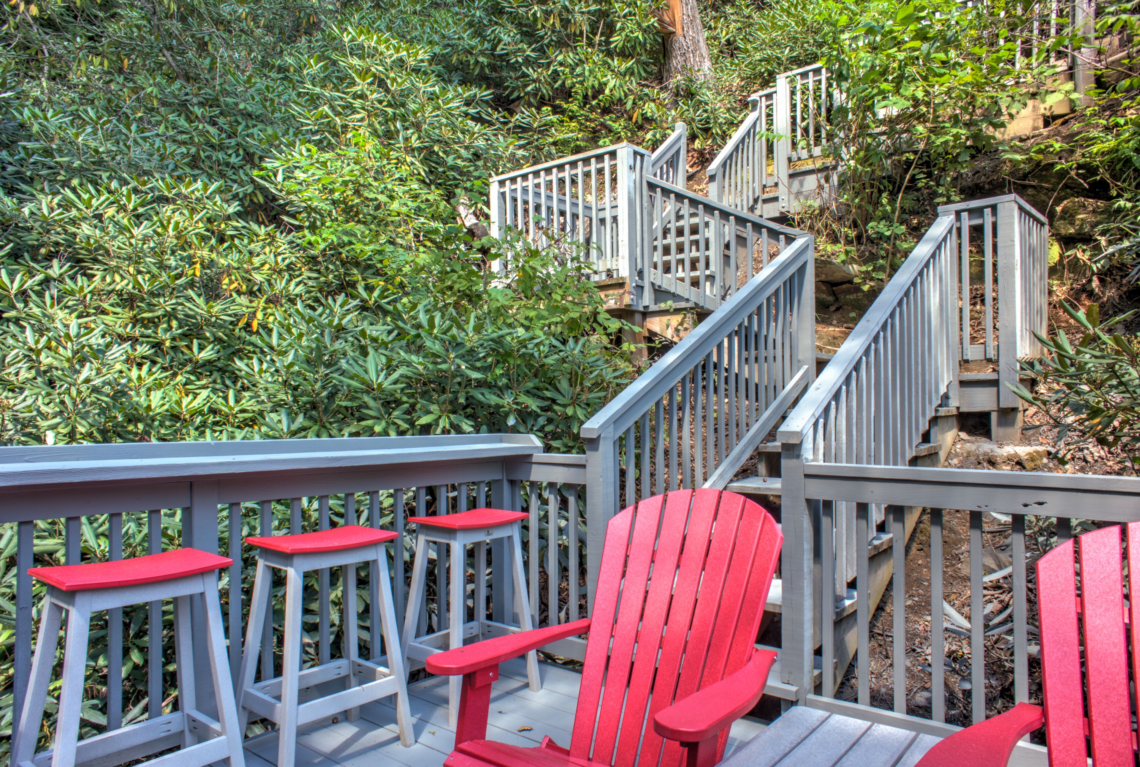 A wooden deck with red Adirondack chairs and a staircase leading to a higher level.