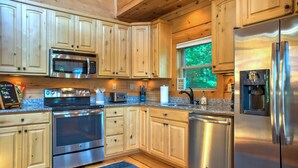 Une cuisine moderne avec des meubles en bois, des appareils électroménagers en acier inoxydable et une fenêtre donnant sur un paysage verdoyant.