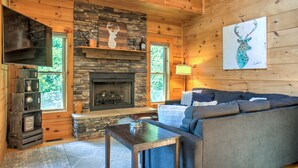 L’intérieur d’un chalet chaleureux, avec une cheminée en pierre, des murs en bois, un canapé et un téléviseur.