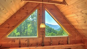 Une cabane en bois dotée de deux grandes fenêtres donnant sur un paysage montagneux boisé.