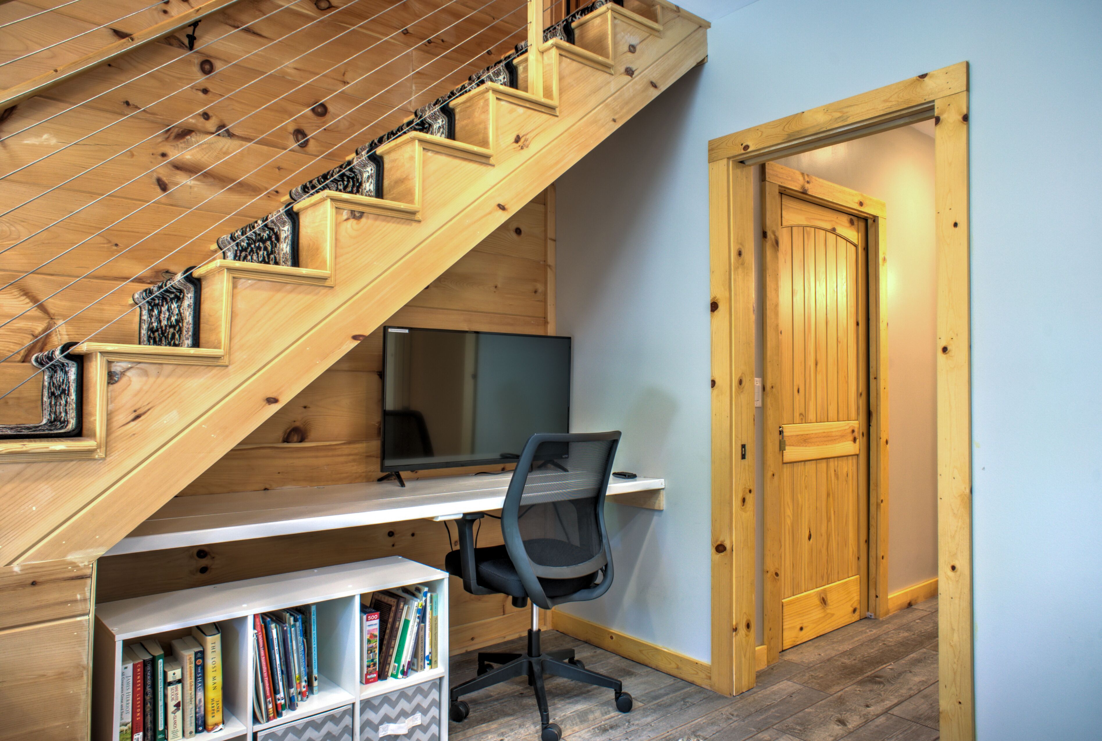 A room with a wooden staircase, a desk with a computer, and a bookshelf.