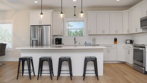 Una cocina moderna con armarios blancos, un refrigerador de acero inoxidable, un horno empotrado y tres taburetes negros.
