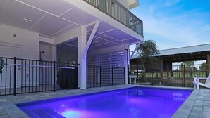 Una piscina con zona cubierta, un edificio blanco con balcón y un patio cercado.