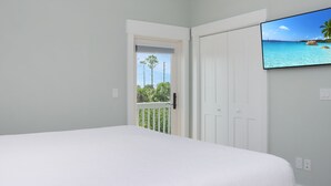 Un dormitorio con una cama, una puerta y un televisor que muestra una escena de playa.