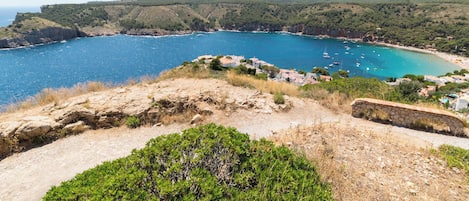 A coastal view with a clear sky, a rocky foreground, and a village with buildings near the sea.