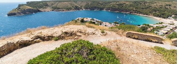 Blick auf die Küste mit blauem Meer, einem felsigen Vordergrund und einem Dorf mit Häusern entlang der Küstenlinie.