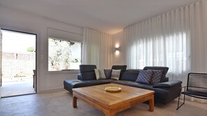 Un salon moderne avec un canapé en cuir foncé, une table basse en bois et une grande fenêtre ornée de rideaux légers.