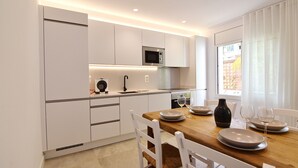 Een moderne keuken met witte kasten, een houten eettafel en uitzicht buiten door een raam.
