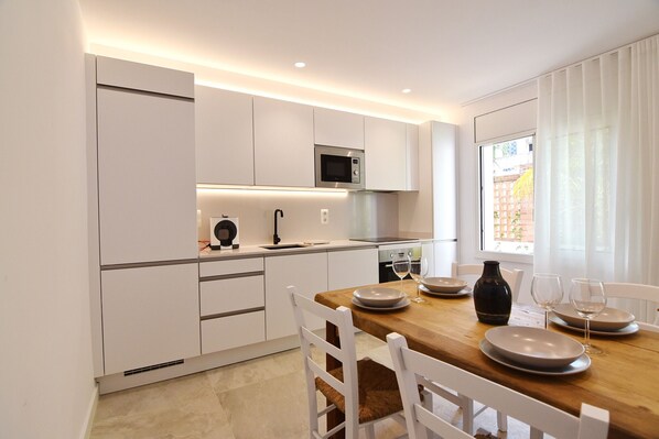 Een moderne keuken met witte kasten, een houten eettafel en uitzicht buiten door een raam.