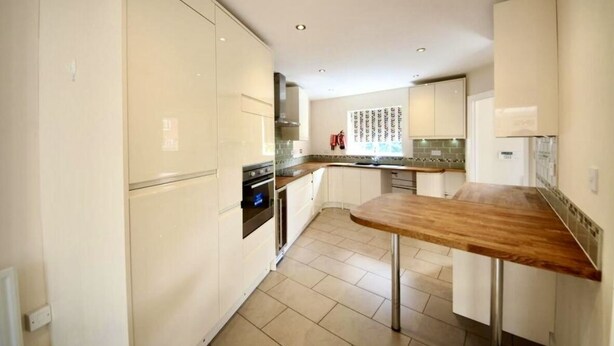 A modern kitchen with white cabinetry, a wooden countertop, and a tiled backsplash.