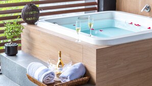 A spa area with a bathtub, two glasses of champagne, a bottle of champagne, a towel, and a potted plant.