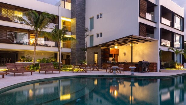 A modern hotel with a swimming pool, outdoor seating, and a bar area.