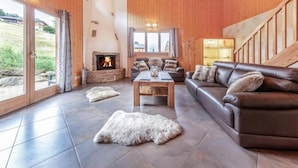 A spacious living room with a fireplace, leather sofa, and a large window offering a view of the outdoors.