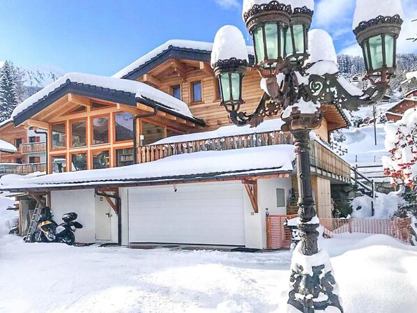 A wooden chalet with a garage and a snow-covered roof.