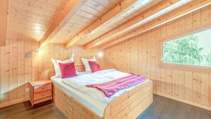 A wooden cabin bedroom with a bed, nightstand, and a window with a view of greenery.