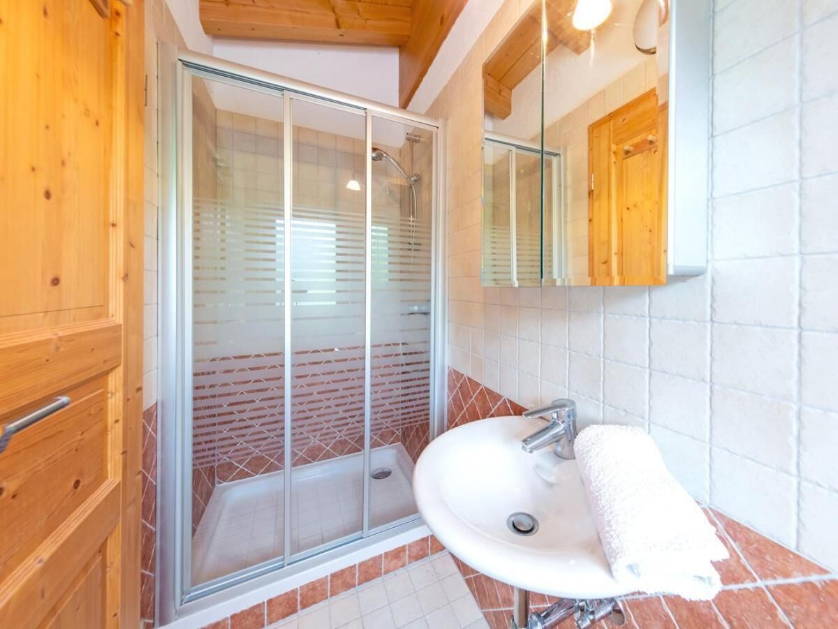 A bathroom with a glass-enclosed shower, a sink with a towel, wooden cabinets, and a tiled wall.