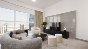Een moderne woonkamer met een bank, salontafel en poufs, een televisie op een zwarte standaard, en een groot raam met uitzicht op de stad.