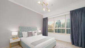 Une chambre à coucher avec un grand lit, une table de chevet, une lampe et une vue sur de hauts immeubles par la fenêtre.