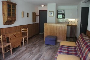 Un espacio habitable compacto con una mesa de madera, dos sillas, un sofá, una pequeña cocina con microondas y un armario.
