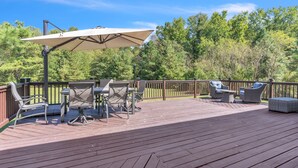 A wooden deck with outdoor furniture, including chairs and a table, under a large umbrella. - Leo Farm Villa - Beautiful Country Retreat 5 Bedroom Villa by RedAwning (Bel Alton)