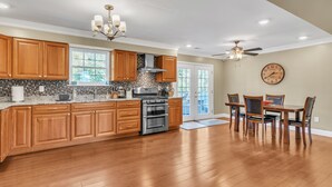A spacious kitchen with wooden cabinets, a large island, stainless steel appliances, and a dining area with a wooden table and chairs. - Leo Farm Villa - Beautiful Country Retreat 5 Bedroom Villa by RedAwning (Bel Alton)