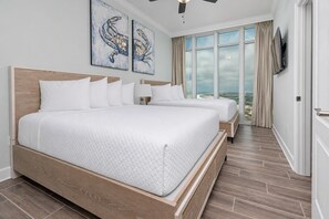 A hotel room with a large bed, two bedside tables, a TV, and a view of the beach.