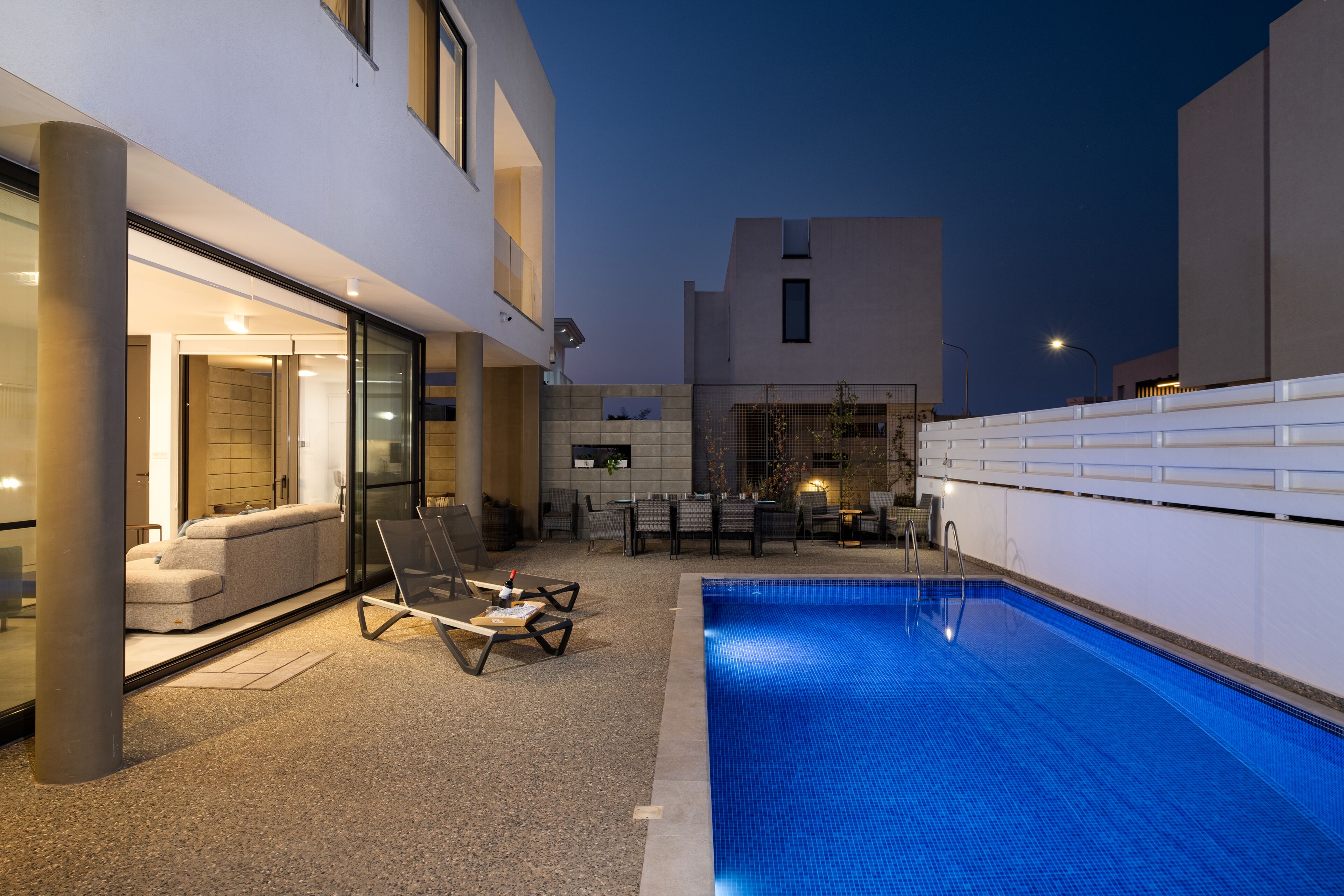 A modern outdoor pool area with a lounge chair and a sofa, a small table, and a dining set.